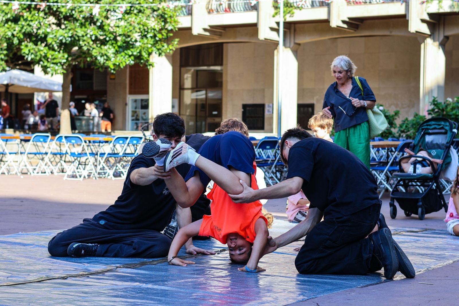 Dos monitores de Space Breaking ayudando a una niña a hacer el pino en una plaza